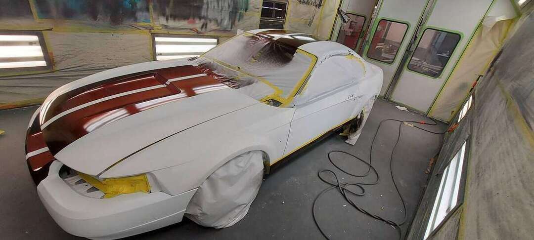 White 1999 Mustang GT masked in a paint booth for burgundy stripes