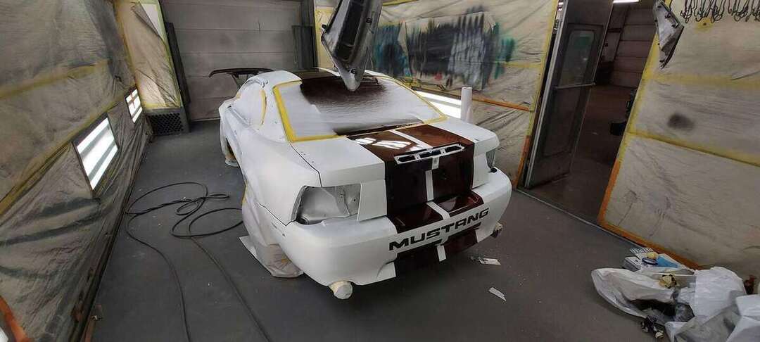 Rear of a masked Mustang GT as burgundy center stripes are painted